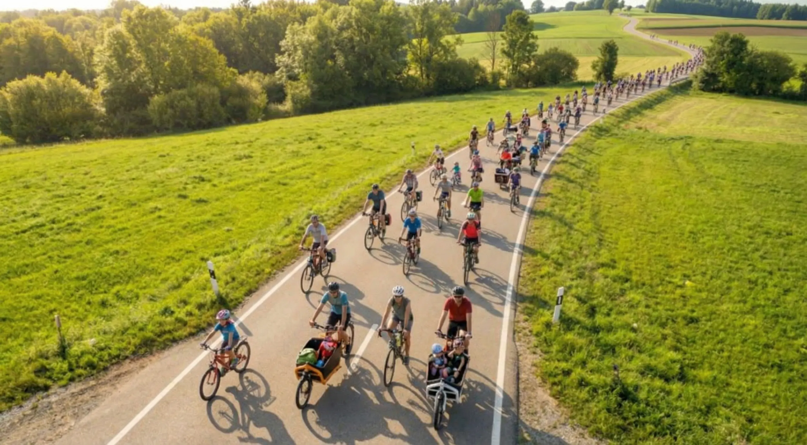 Drohnenaufnahme in geringer Höhe: verschiedene Radfahrende auf einer Landstraße in süddeutscher Sommerlandschaft